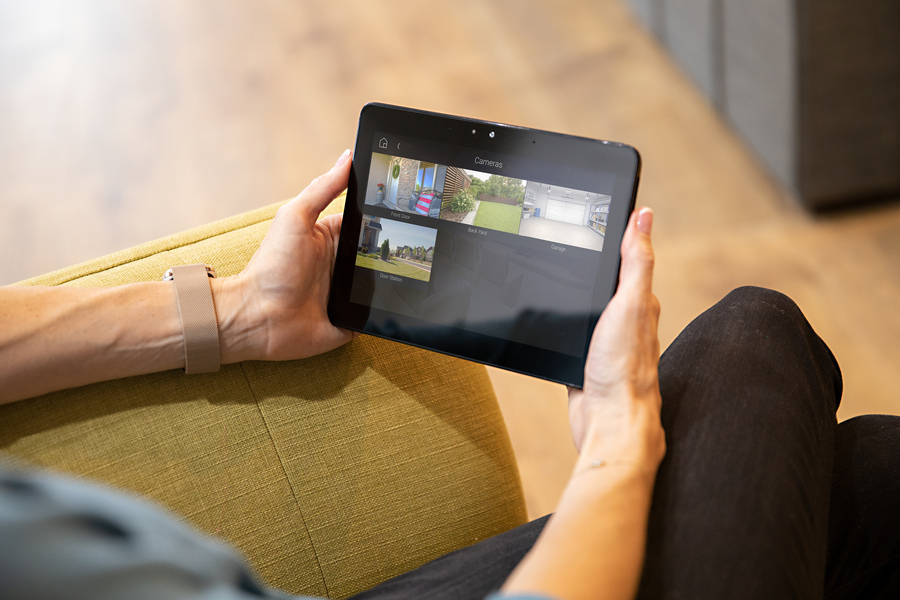 Person using a tablet to view multiple home surveillance camera feeds from different areas, like the garage and yard.